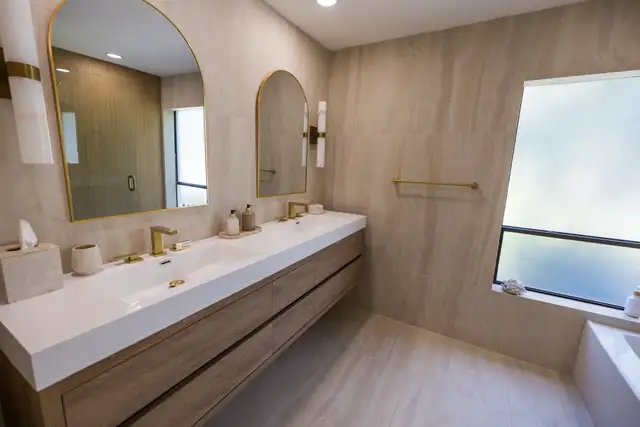 Renovated bathroom in Boca Raton, FL with a floating wood double vanity, arched brass mirrors and large-format beige porcelain walls