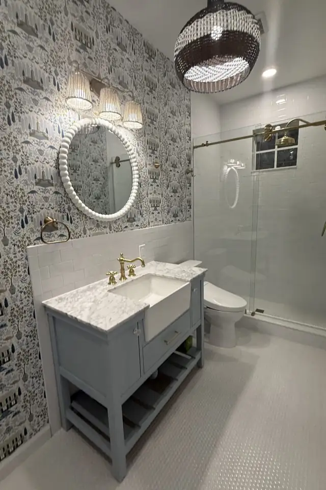 Bathroom remodel with botanical wallpaper, gray furniture vanity with marble top, brass faucet and glass shower