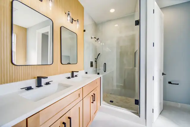 Bathroom with light wood double vanity, black faucets, two framed mirrors and frameless glass shower